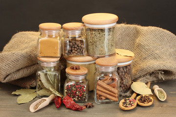 jars and spoons with spices on wooden table on black background