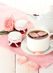 teapot and cup of tea with roses and jam on white wooden table