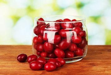 fresh cornel berries in glass jar on green background close-up