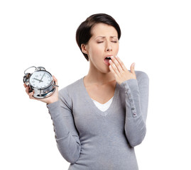 Yawning pretty woman holds an alarm clock, isolated on white
