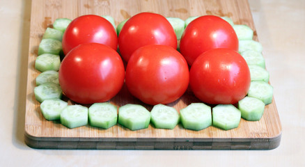 Fresh cucumbers and tomatoes on a wood chopping board