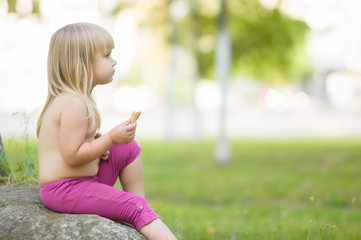 Naklejka na ściany i meble Adorable girl eat ice cream sitting on stone in park