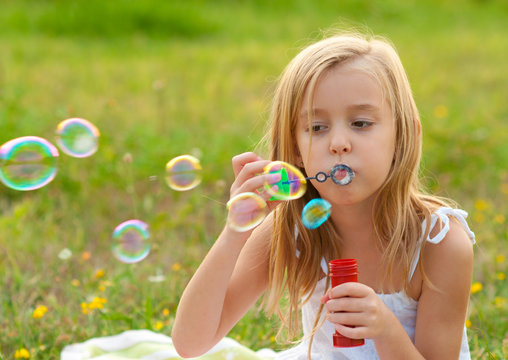 Cute little girl blowing soap bubbles on the meadow