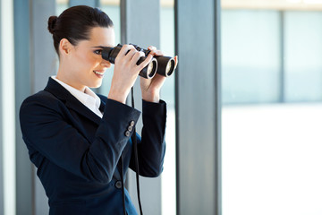 businesswoman looking outside office window with binoculars