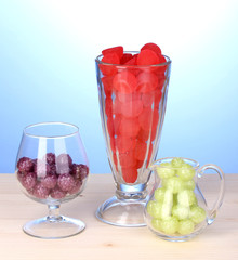 Color candies in glasses on wooden table on blue background