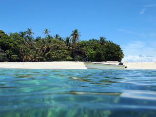 Caribbean beach on a island with tropical vegetation and a boat on the sea shore, seen from water surface