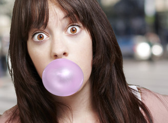 Naklejka premium young girl with a pink bubble of chewing gum against a street ba