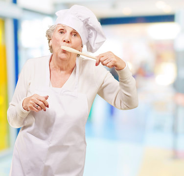 portrait of cook senior woman with wooden spoon on mouth indoor