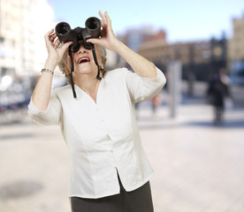 portrait of senior woman looking through a binoculars at city