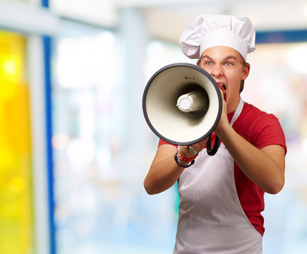 portrait of young cook man screaming with megaphone indoor