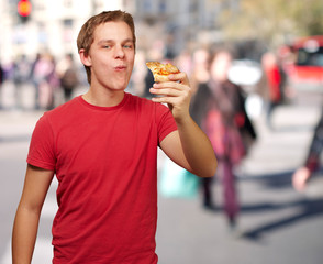 portrait of young man eating pizza portion at crowded street