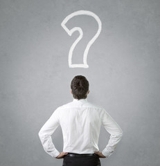 Confused, young businessman looking at question mark