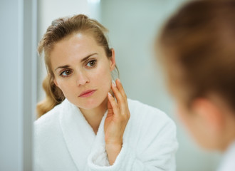 Obraz na płótnie Canvas Młoda kobieta w szlafroku sprawdzania jej twarz w lustrze w łazience