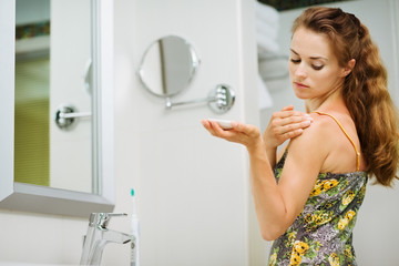 Young woman applying body creme on shoulder in bathroom