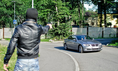 Man in mask pointing gun toward car. Robbery concept