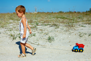 cute baby boy dragging toy car walking at the field