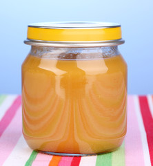 Jar of baby puree on napkin on blue background