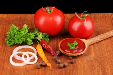 Ketchup and ripe tomatoes on wooden table on black background