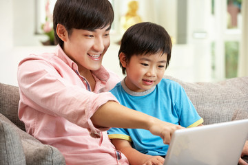 Chinese Father And Son Using Laptop Whilst Relaxing On Sofa