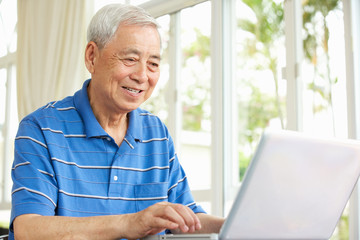 Fototapeta na wymiar Starszy Chińczyk Posiedzenia Na Biurko Korzystanie z laptopa w domu