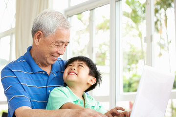 Chinese Grandfather And Grandson Sitting At Desk Using Laptop