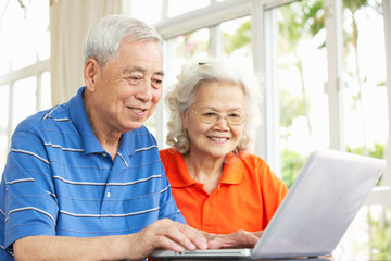 Senior Chinese Couple Sitting At Desk Using Laptop At Home