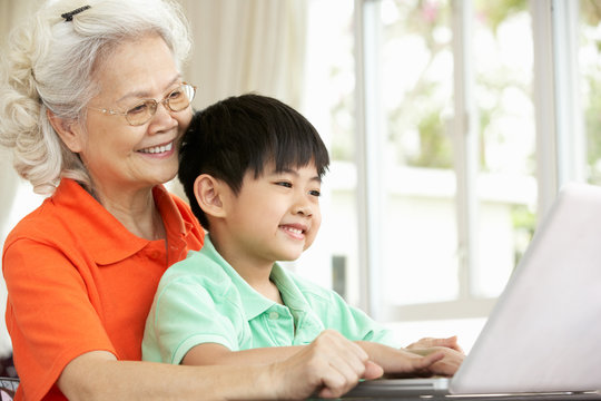 Chinese Grandmother And Grandson Sitting At Desk Using Laptop