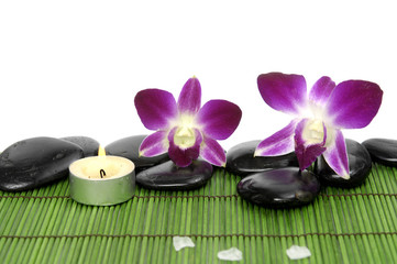 burning candle and massage stones with orchid on mat