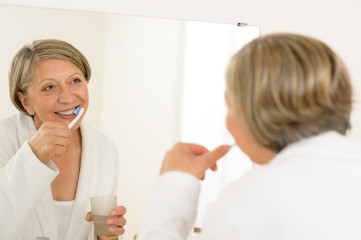 Obraz na płótnie Canvas Mature woman brushing teeth look bathroom mirror