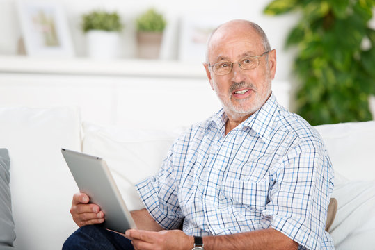 älterer mann sitzt mit tablet-pc auf dem sofa