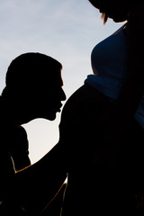 Contraluz de beso de un padre a su hija aún dentro de la tripa de su madre embarazada