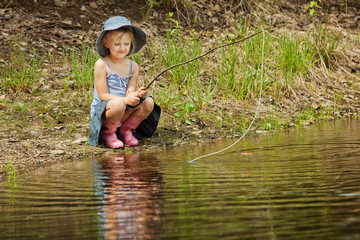 Little girl are fishing on lake in forest