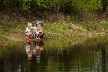 Fototapeta na wymiar Little girls are fishing on lake in forest