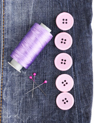 Colorful sewing buttons with thread on jeans isolated on white