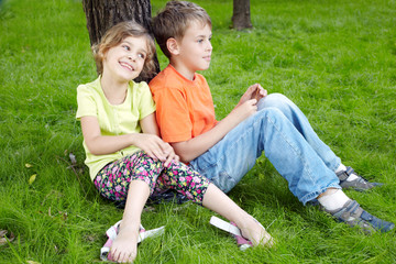 Fototapeta premium Boy sits on grass and sister sits nearby
