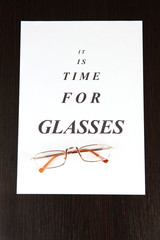 Eyesight test chart with glasses on wooden background close-up