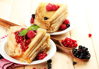 Delicious pancakes with berries, jam and honey on wooden table