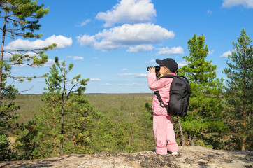 Little girl looking through binoculars from a high mountain