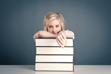 Young girl student with pile of books against dark background.