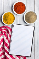various colored spices with blank recipe book
