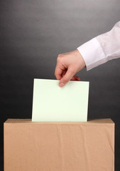 Hand with voting ballot and box on grey background