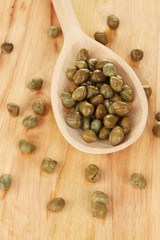 green capers in wooden spoon on wooden background close-up