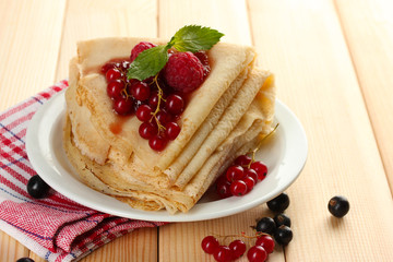 Delicious pancakes with berries and jam on plate on wooden
