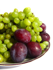 Green grapes and plums on a plate isolated on white background c
