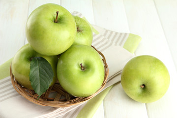 Ripe green apples with leaves in basket, on wooden table