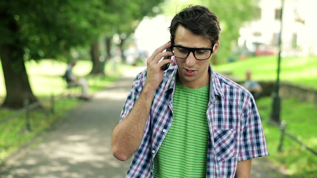 Young man talking on cellphone in the park, steadicam shot