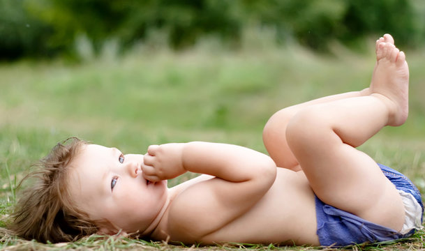 chubby baby in diapers lying on back on grass and dreaming,