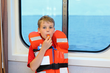 Boy dressed in life jacket blows whistle and stands near window
