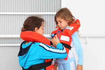 Mother dresses her daughter in orange life jacket at deck