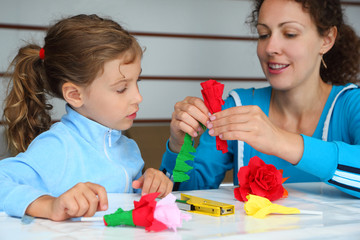 Obraz na płótnie Canvas Happy mother and daughter make artificial roses of tissue paper;